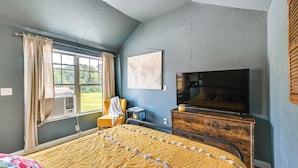 Une chambre à coucher avec un lit, une télévision, une commode et une fenêtre avec des rideaux.