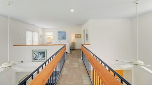 Un couloir d’hôtel avec une rambarde en bois, un sol recouvert de moquette et un ventilateur de plafond.