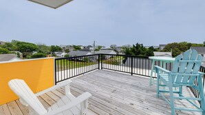 Une terrasse en bois avec un mur jaune, une rambarde noire et deux chaises Adirondack bleu clair.