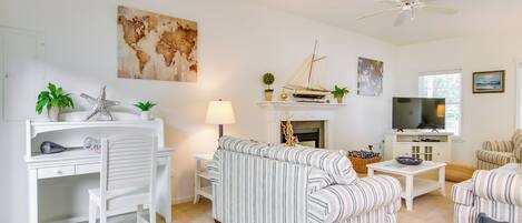 A living room with a striped sofa, a white desk, a television, and a fireplace.