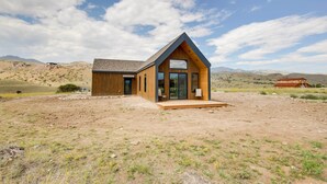 A modern wooden cabin with a sloped roof and large windows, situated in a dry, hilly landscape. - Yellowstone Prairie Retreat: 360 Mountain Views! (Emigrant)