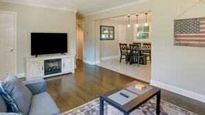 A living room with a flat-screen TV, a gray sofa, a coffee table, and a dining area with a table and chairs. - Family-friendly Blacksburg Retreat w/ Playground! (Blacksburg)