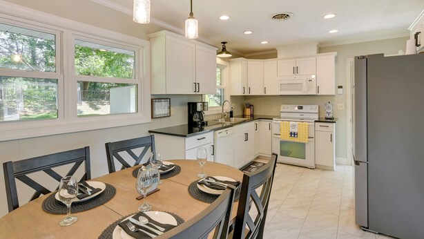 A modern kitchen with white cabinets, a stainless steel refrigerator, and a dining table set for four. - Family-friendly Blacksburg Retreat w/ Playground! (Blacksburg)