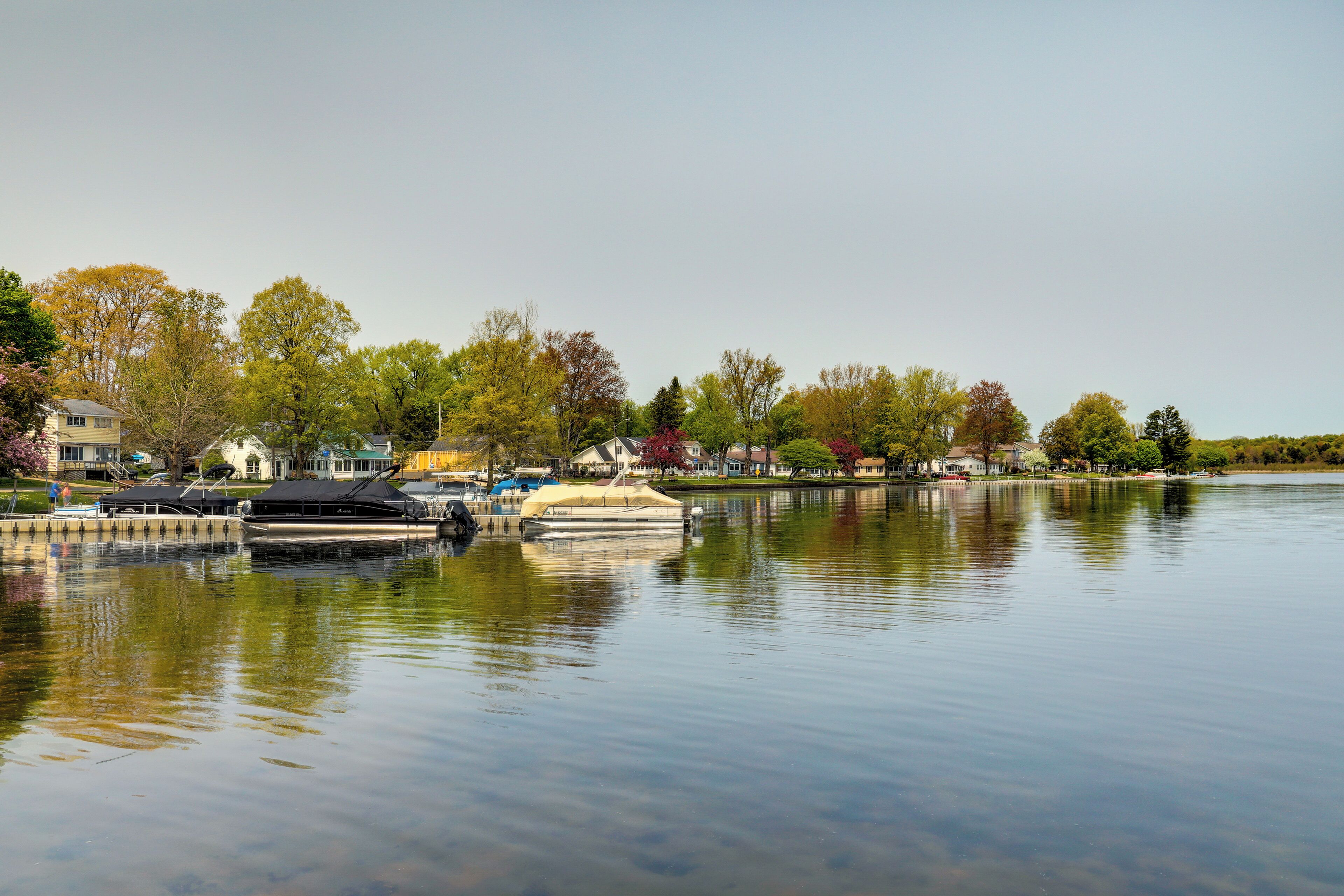 A calm lake with boats docked, surrounded by trees and buildings.