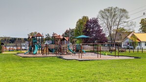 A playground with various play structures, including slides and climbing areas, surrounded by a grassy field and trees. - Walk to Beach, Lake Edinboro Views: 'camp Dickson' (Edinboro)