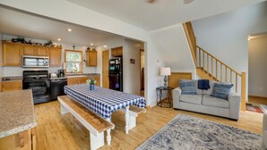 A spacious living area with a kitchen, wooden flooring, a dining table with a checkered tablecloth, a sofa, and a staircase. - Walk to Beach, Lake Edinboro Views: 'camp Dickson' (Edinboro)