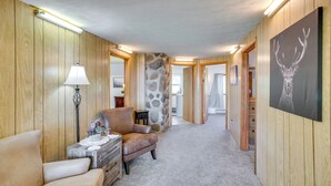 A hallway with wooden walls, a stone accent wall, a brown leather chair, a small table with a lamp, and a framed deer head picture. - Sunny Cedaredge Home w/ Mtn Views - Hike & Fish! (Cedaredge)