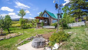 A house with a stone foundation, a green roof, and a wooden deck. - Sunny Cedaredge Home w/ Mtn Views - Hike & Fish! (Cedaredge)