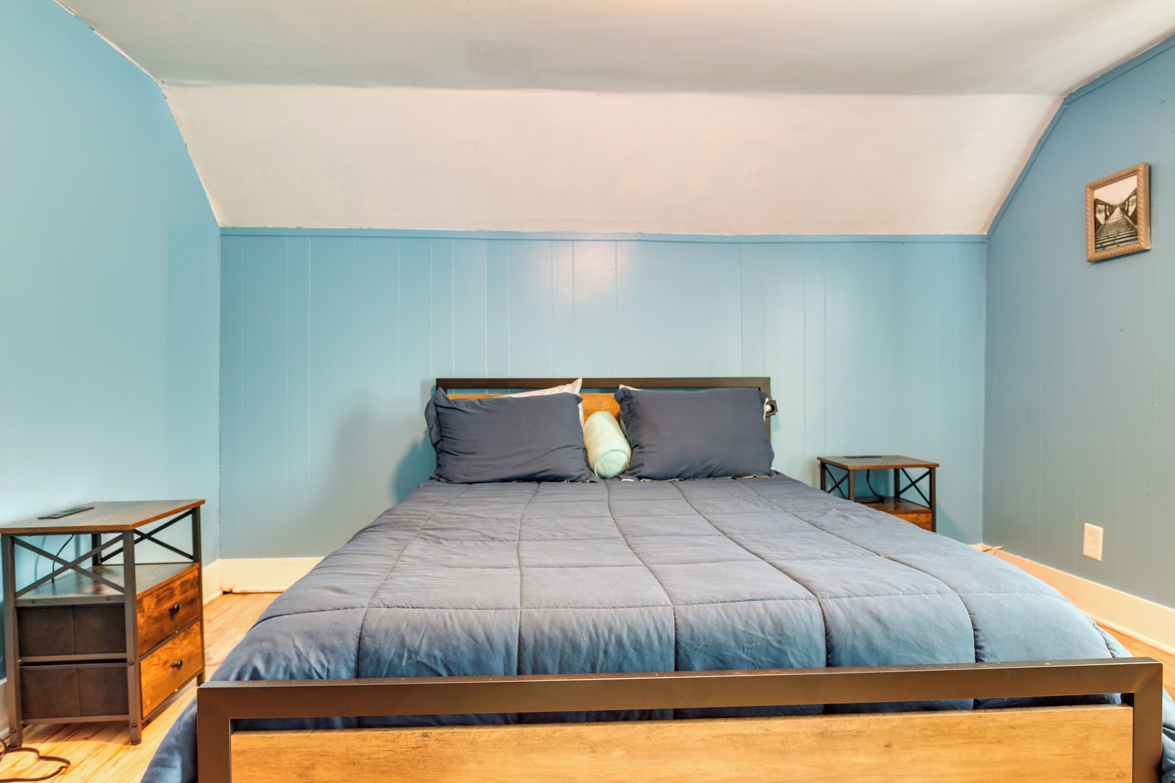 Quarto com estrutura de cama de madeira, parede azul e pequena mesa de cabeceira de madeira.