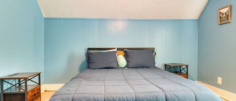 Quarto com estrutura de cama de madeira, parede azul e pequena mesa de cabeceira de madeira.