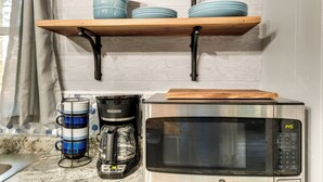 A kitchen with a stainless steel microwave, a coffee maker, and a shelf with blue plates. - Pet-friendly Michigan Getaway w/ Porch & Kayaks! (Ontonagon)