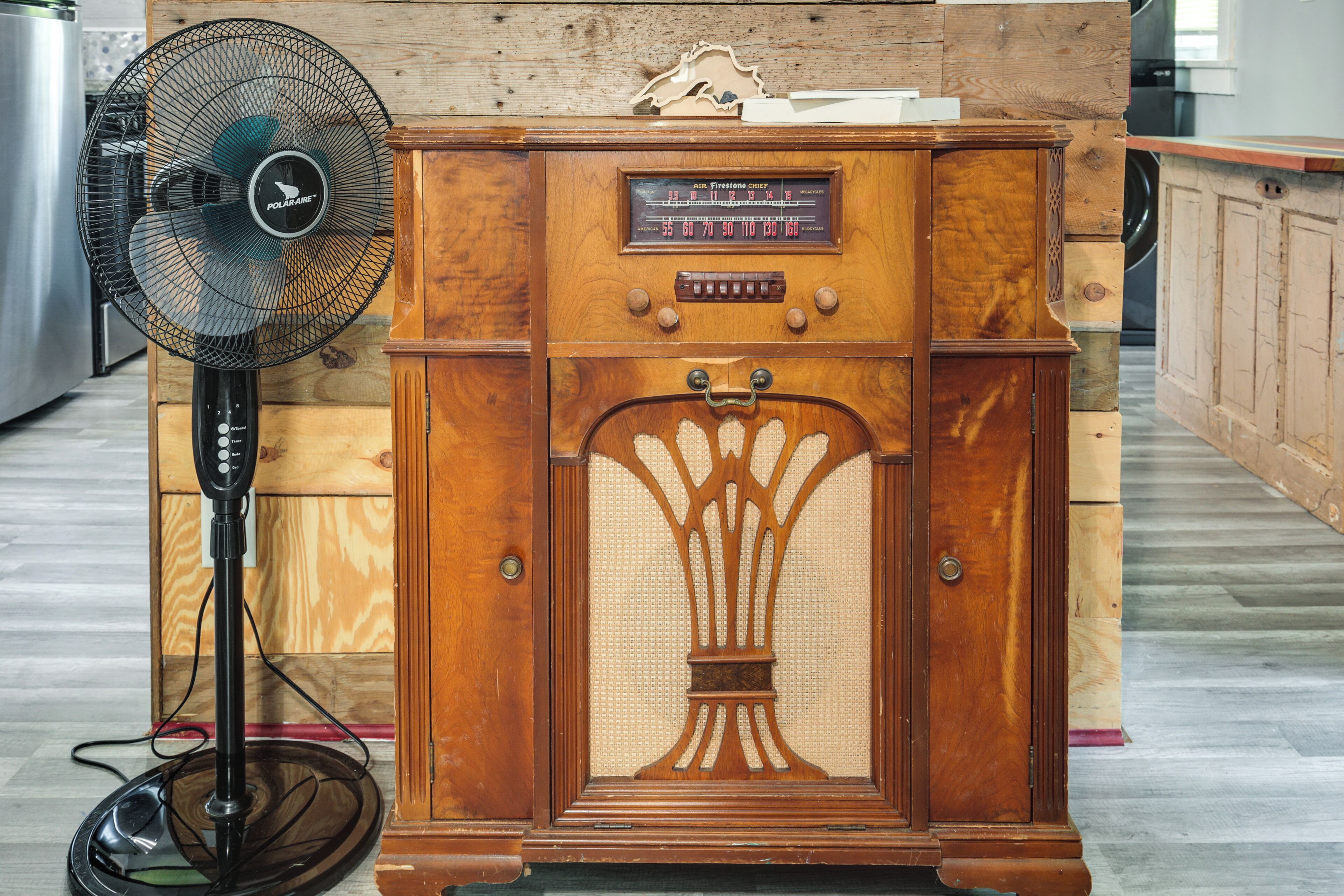 Una radio antigua y un ventilador de pie en una habitación con muebles de madera y suelo de baldosas.