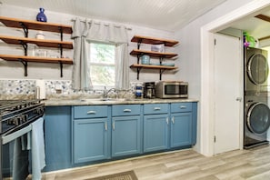 A kitchen with blue cabinets, a stove, a microwave, and a washing machine.