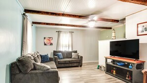 A living room with a sofa, a television on a wooden stand, and a decorative item on the wall. - Pet-friendly Michigan Getaway w/ Porch & Kayaks! (Ontonagon)