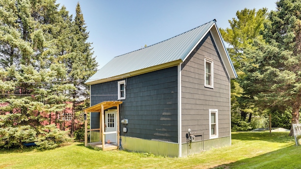 A two-story house with a dark gray exterior, a sloped roof, and a small porch with a wooden railing. - Pet-friendly Michigan Getaway w/ Porch & Kayaks! (Ontonagon)