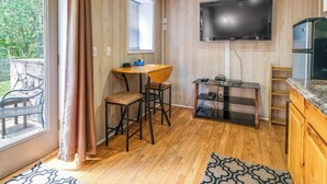 A compact kitchen with a wooden floor, a TV mounted on the wall, a refrigerator, and a dining area with a table and chairs. - Cozy Hiwassee Vacation Rental w/ Yard (Hiwassee)
