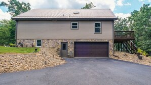 A two-story house with a stone facade, a dark garage door, and a covered porch with a staircase. - Cozy Hiwassee Vacation Rental w/ Yard (Hiwassee)