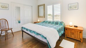 Un dormitorio con cama, una silla, mesita de noche, espejo y ventana con persianas.