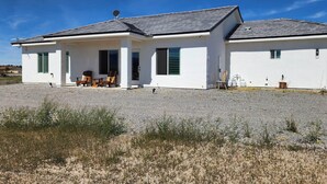 Una casa de dos pisos con entrada de grava, un patio con mobiliario exterior y una antena parabólica en el techo.