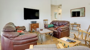 Un salón con un sofá de cuero marrón, una mesa de centro de madera y un televisor montado en la pared.