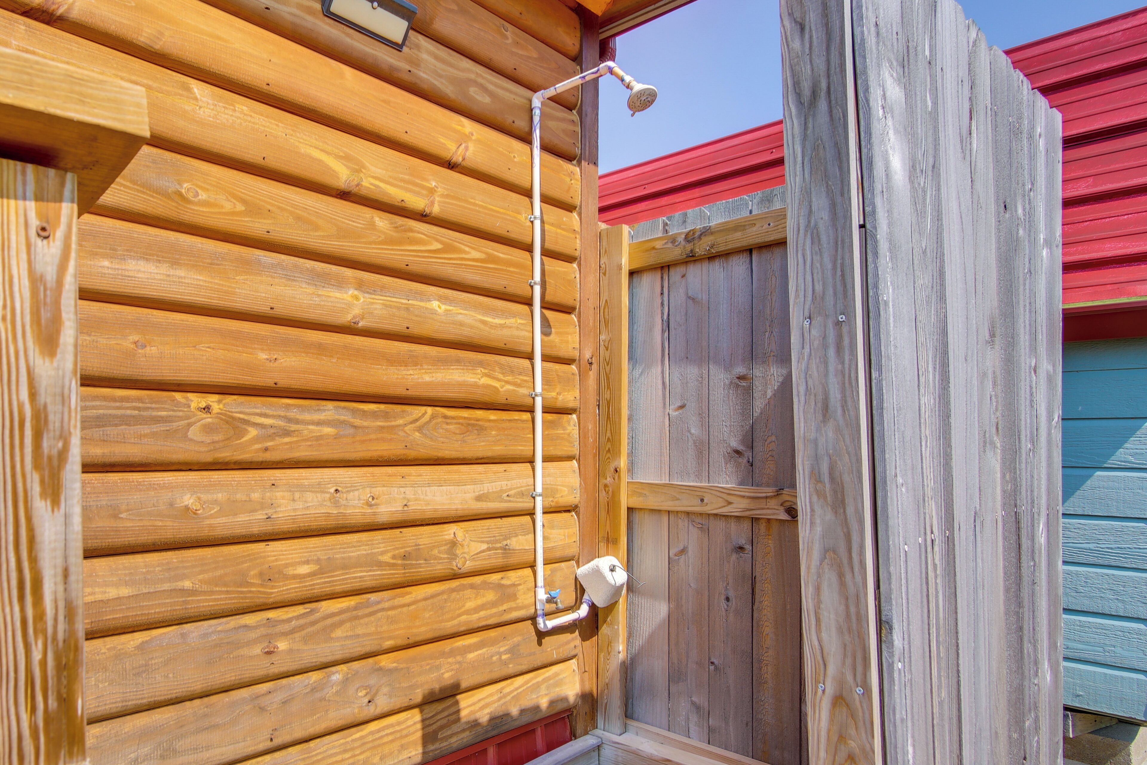 Una cabaña de madera con un cabezal de ducha metálico sujeto a la pared exterior.