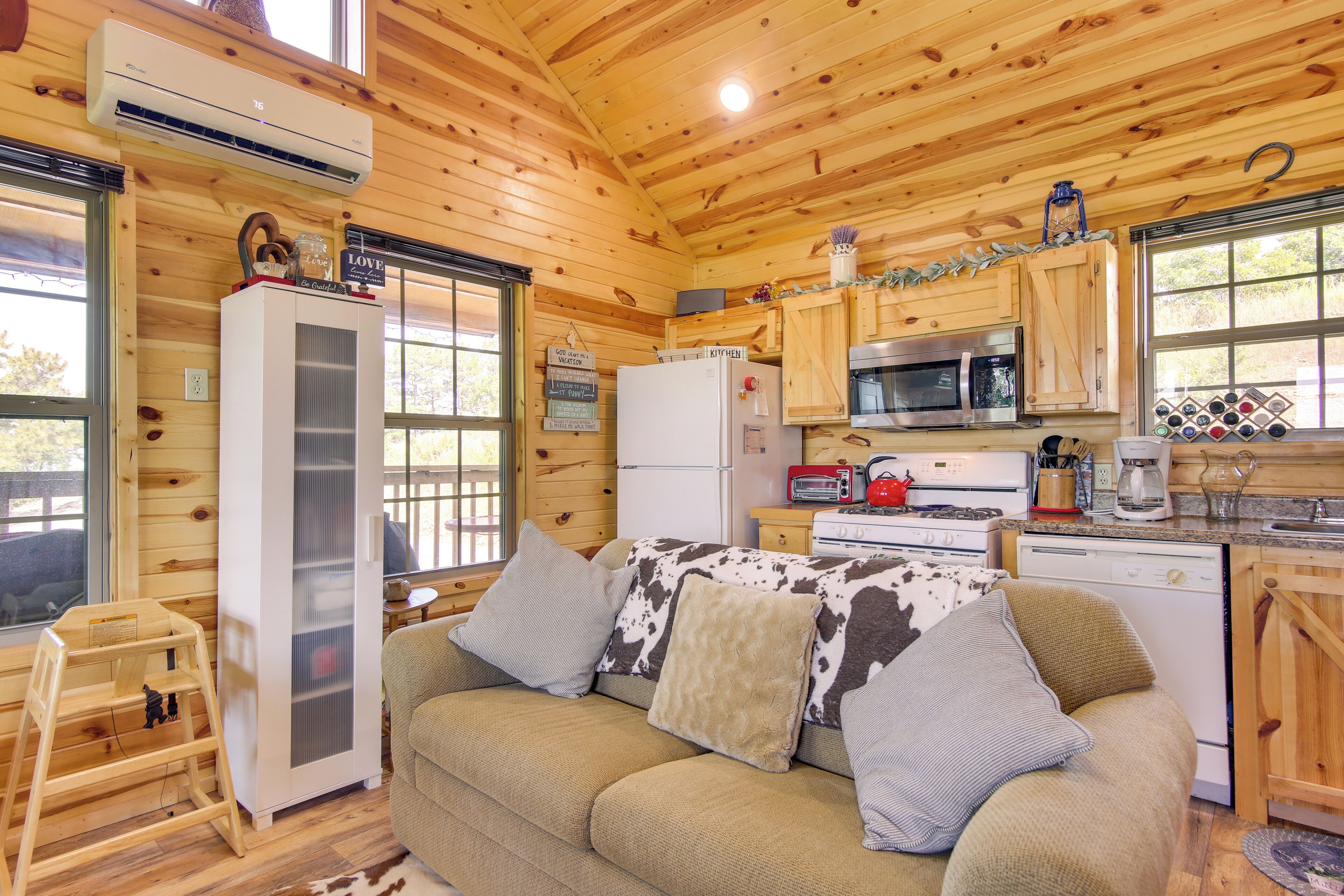 A cozy cabin interior with a wooden interior, a kitchenette with a microwave, stove, and refrigerator, and a sofa with cowhide pillows.