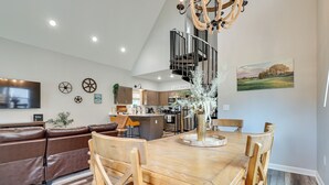 Eine moderne Küche mit Kochinsel, ein Essbereich mit Holztisch und -stühlen, eine eingebaute Sitzecke mit braunem Ledersofa und eine Wendeltreppe, die in eine obere Ebene führt.
