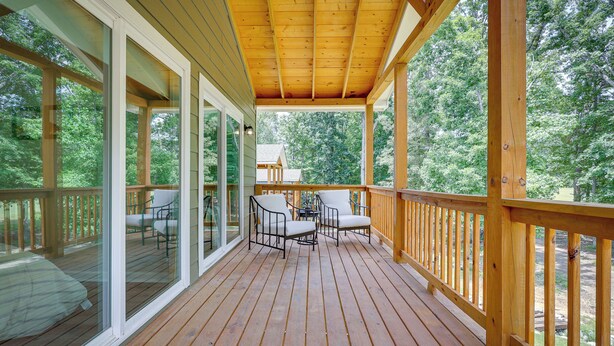 Eine Holzterrasse mit Glastüren, zwei Stühlen und einem kleinen Tisch.