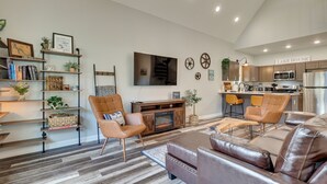 Ein modernes Wohnzimmer mit Kamin, Ledersofas, einer Bücherwand und einer Küche im Hintergrund.