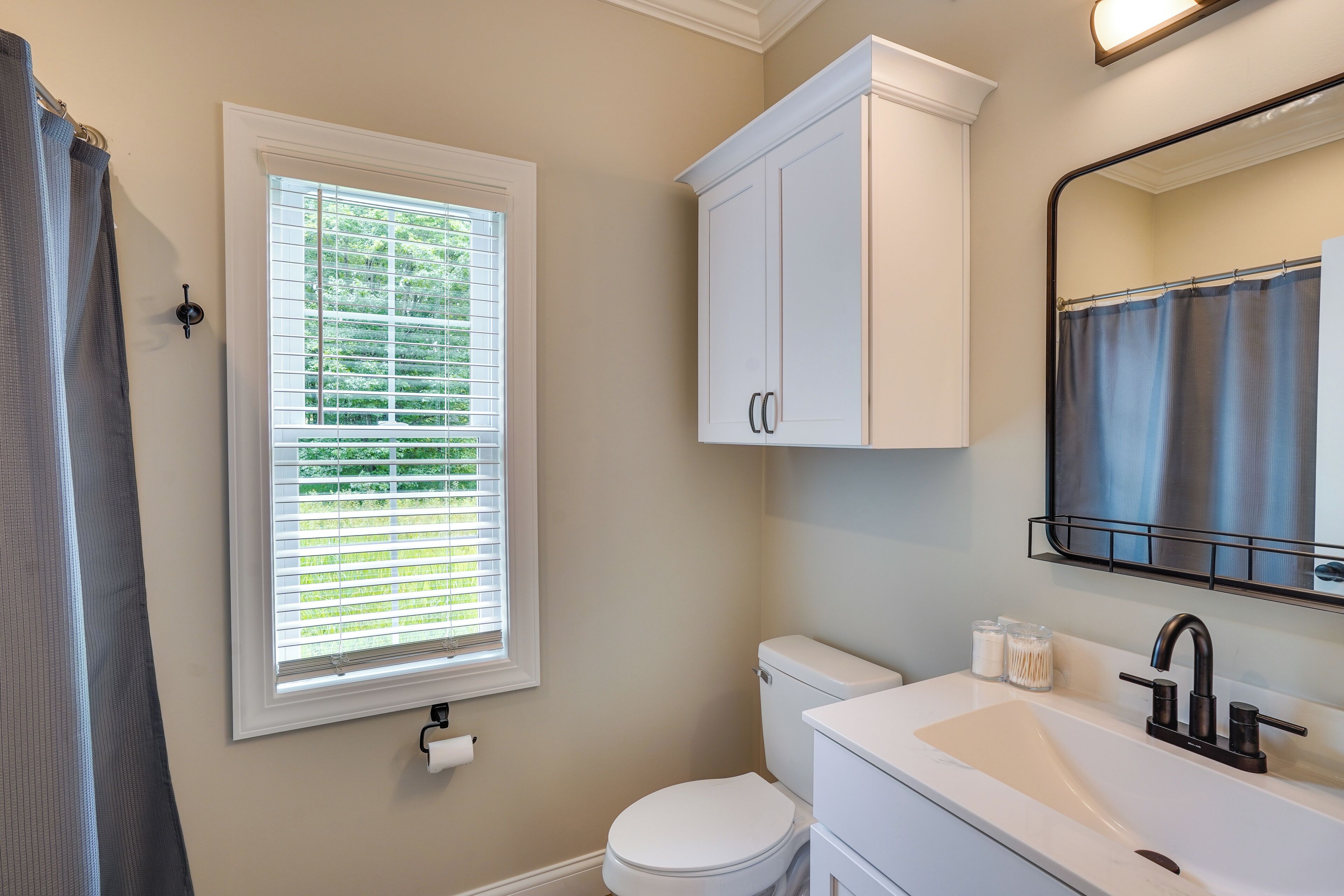 A bathroom with a toilet, sink, and window with blinds.