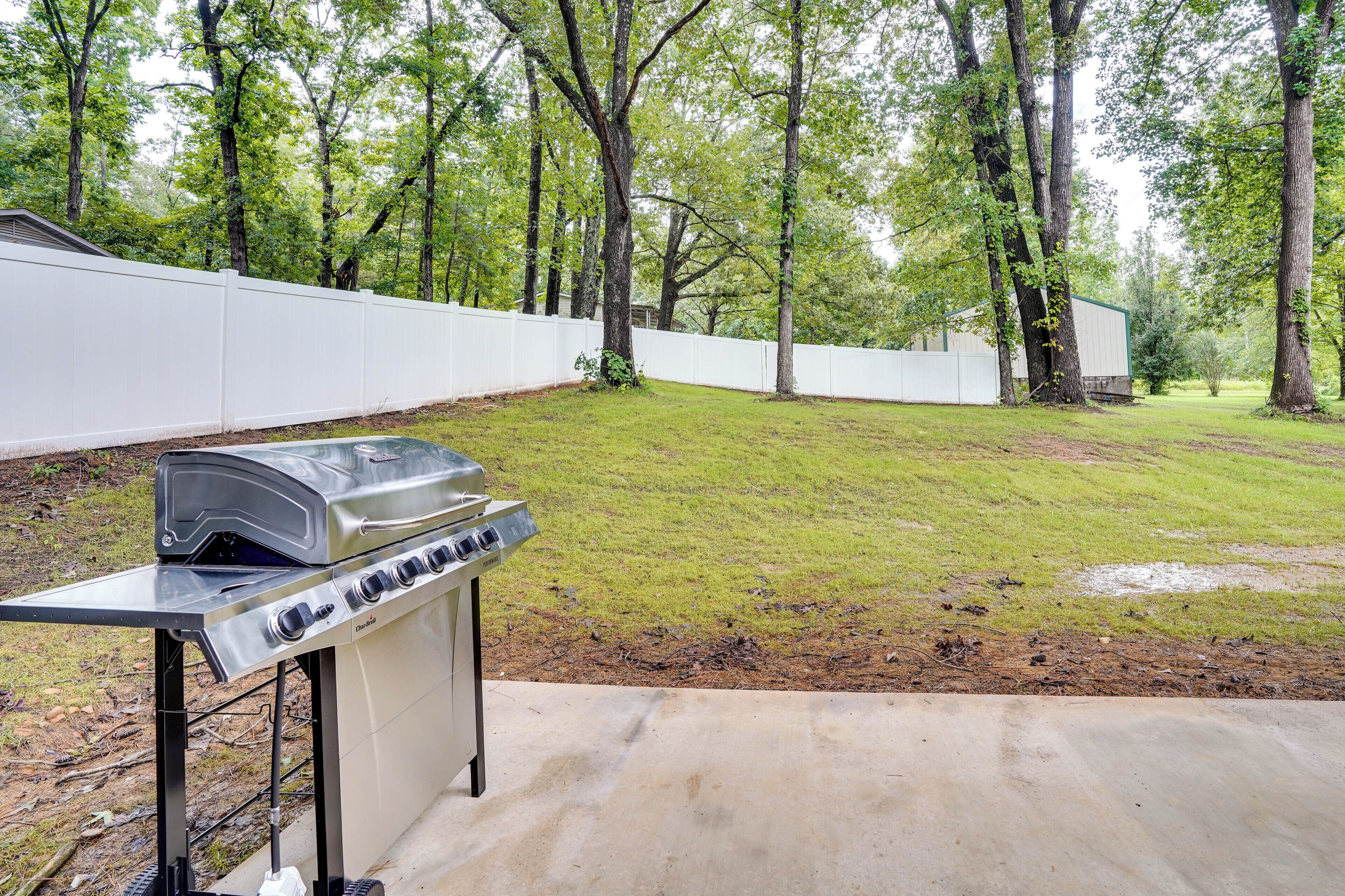 A backyard with a stainless steel grill, a white fence, and a grassy lawn.