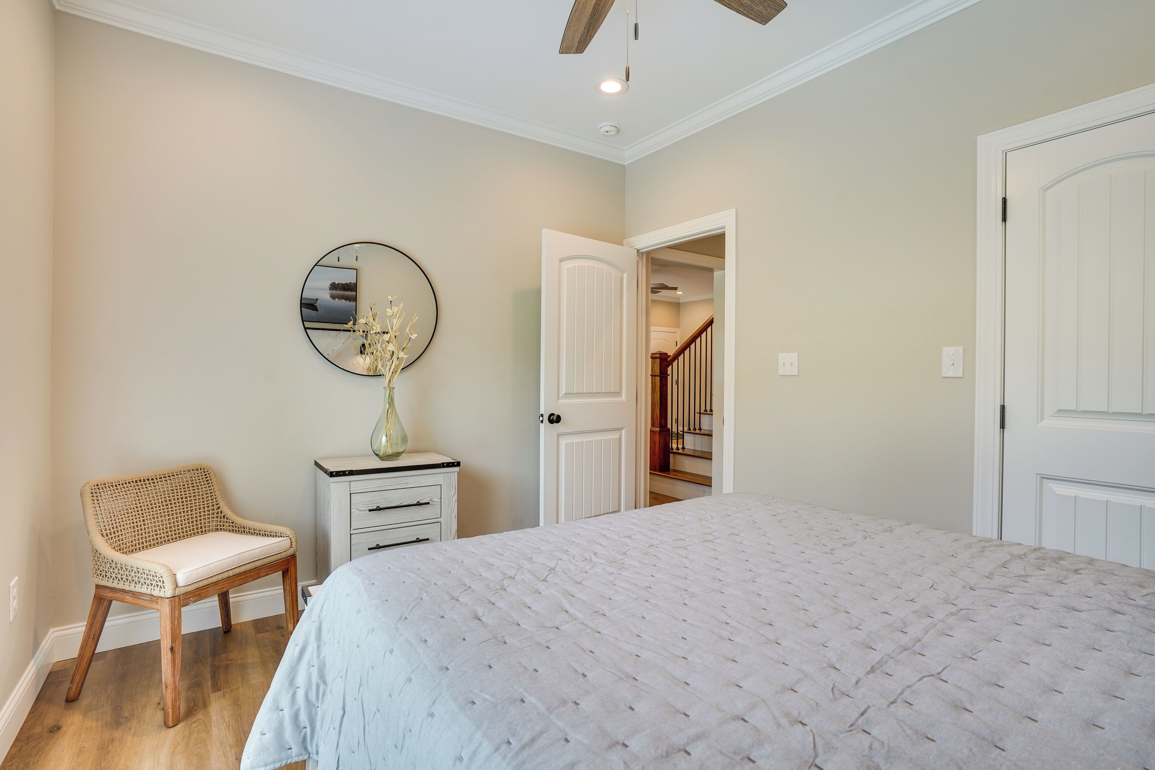 A bedroom with a bed, a chair, a dresser, a mirror, and a door leading to a staircase.