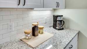 A kitchen with white cabinets, a granite countertop, and a coffee maker. - Boat Ramp Access: Modern Kentucky Lake Home (Hardin)