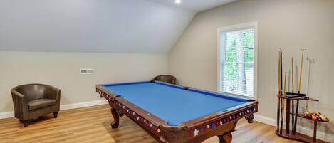 A pool table with a blue felt surface, a brown leather chair, and a pool cue rack with cues and balls.