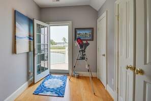 A room with a sliding glass door leading to a balcony, a telescope on a tripod, a framed picture on the wall, and a blue patterned rug. - Bayfront White Stone Escape w/ Private Beach! (White Stone)