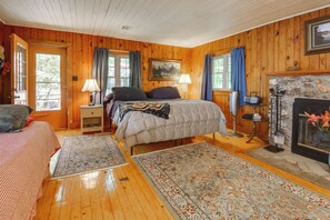 Un dormitorio de cabaña de madera con una cama, dos mesitas de noche, una lámpara, una chimenea y una alfombra.
