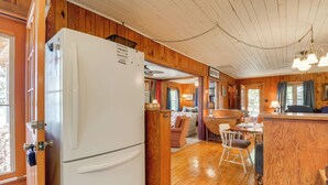 Cocina con paneles de madera, un refrigerador blanco, una zona de comedor con mesa y sillas, y una encimera de madera.
