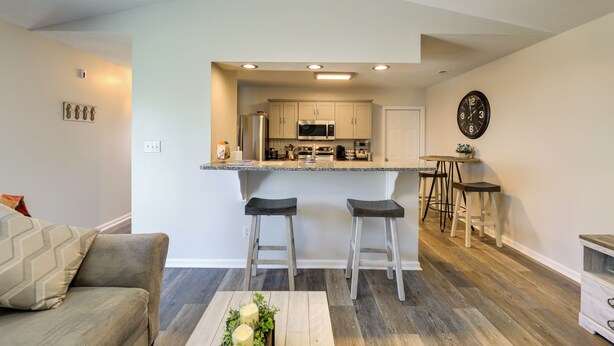Una cocina moderna con una isla central, taburetes de bar y una zona de comedor con un reloj en la pared.