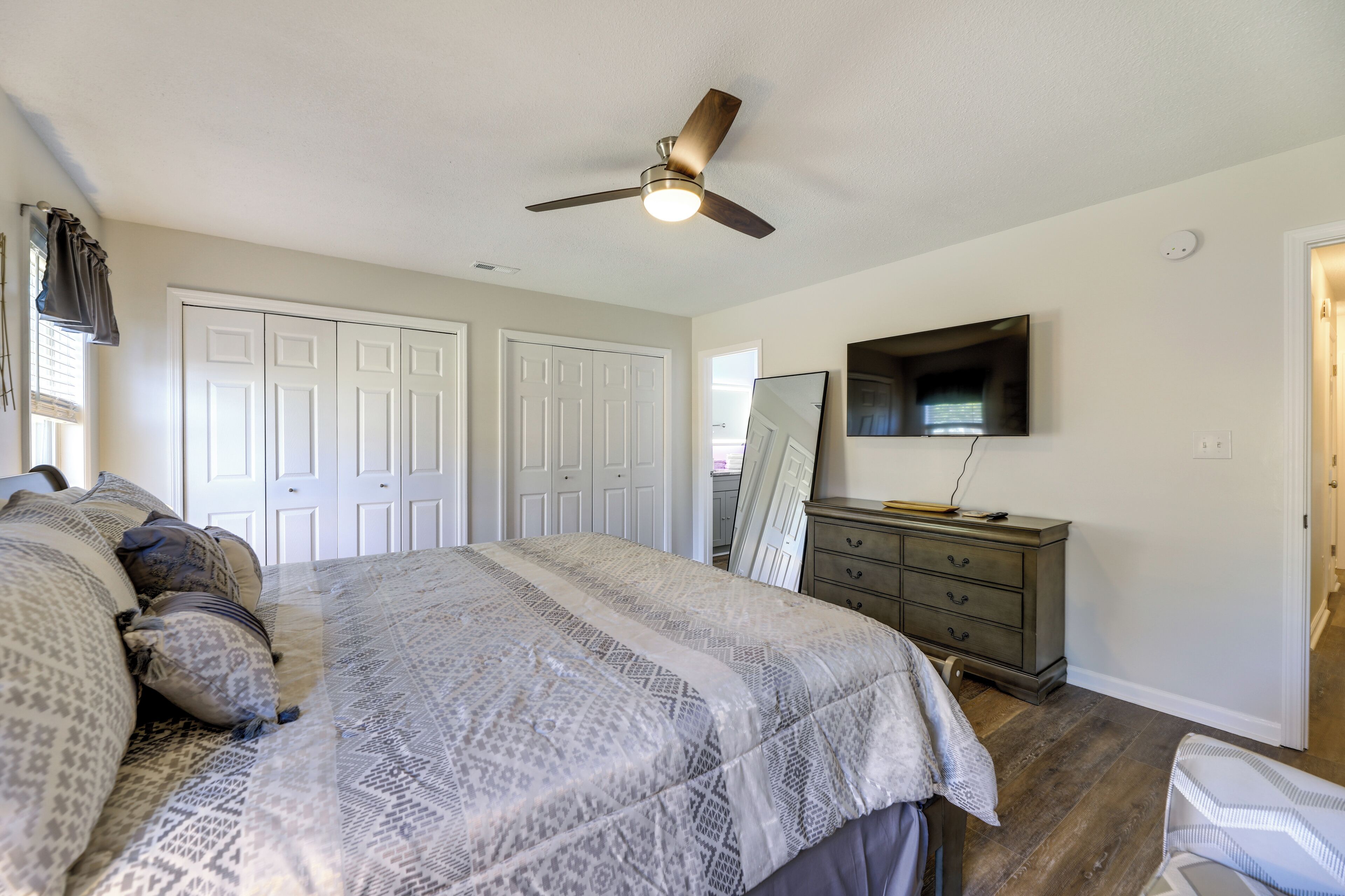 A bedroom with a bed, a ceiling fan, a dresser, and a TV on the wall.