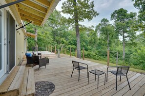 Een houten terras met buitenmeubilair, zoals stoelen en een tafel, met uitzicht op een bebost gebied.