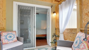 Una stanza con mobili in vimini, una porta scorrevole in vetro che dà su una camera da letto e un lampadario fissato alla parete.