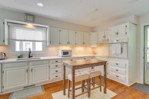 A kitchen with white cabinets, a wooden table with two stools, a microwave, and a clock on the wall.