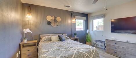 A bedroom with a bed, nightstands, a dresser, a ceiling fan, wall sconces, and a large window.