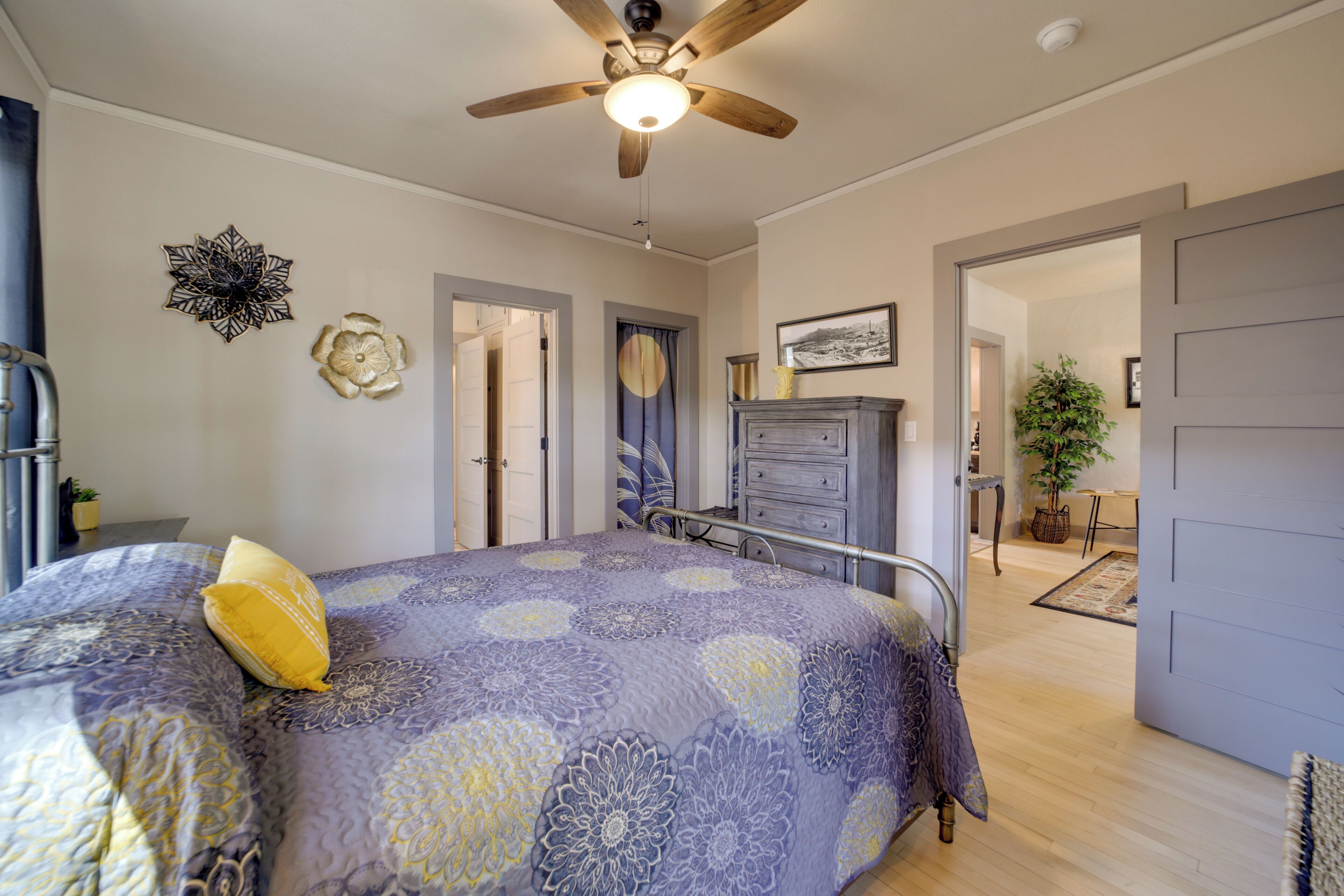 A bedroom with a bed, a ceiling fan, a dresser, and a door leading to another room.