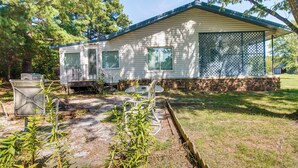 A mobile home with a covered porch, a small patio area with a table and chairs, and a garden with young plants. - Cookson Vacation Rental w/ Spacious Yard & Porch! (Cookson)