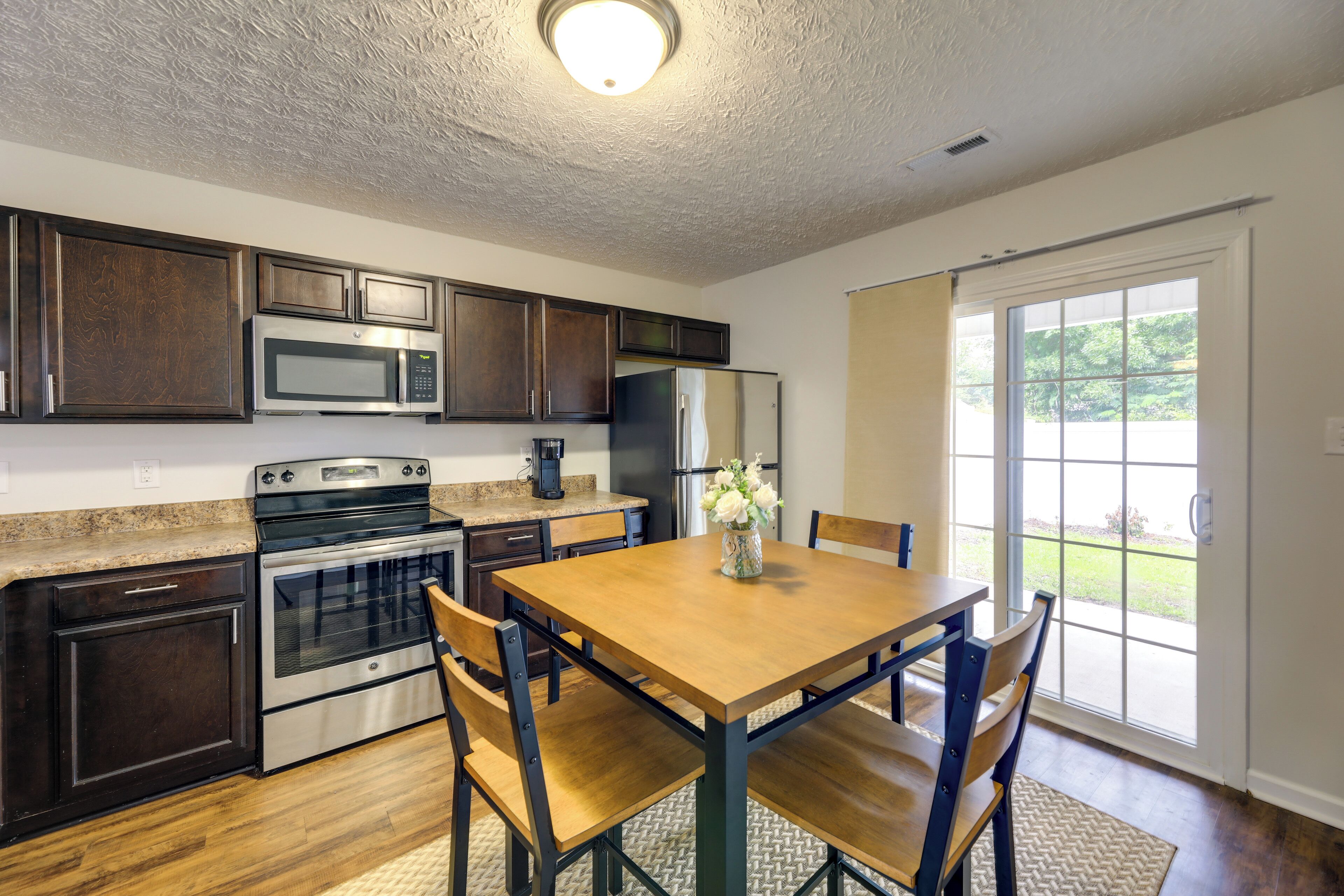 A kitchen with dark wood cabinets, stainless steel appliances, and a wooden dining table with chairs.