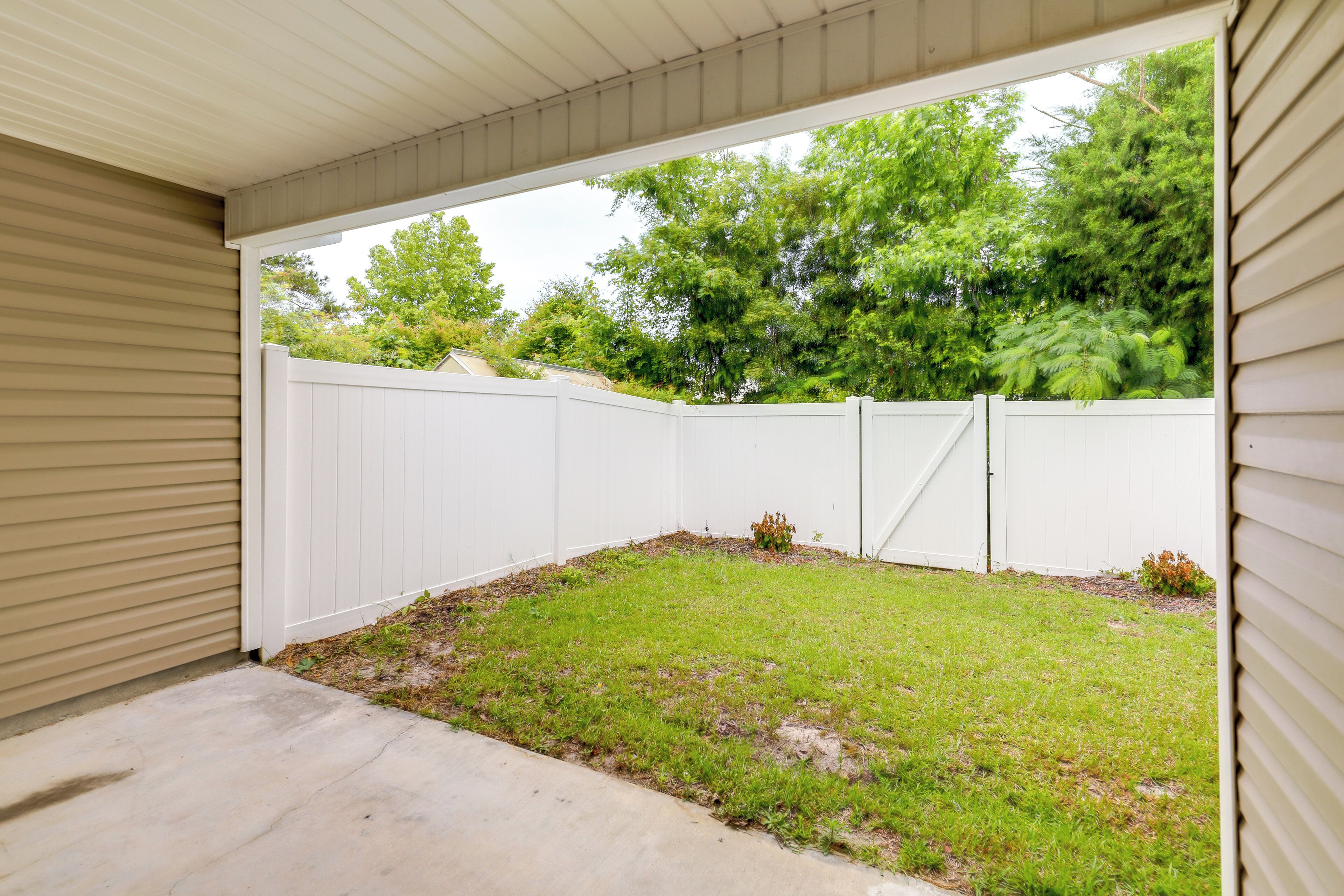 A covered patio area with a white fence and a grassy lawn.