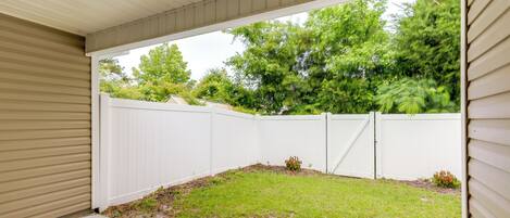 A covered patio area with a white fence and a grassy lawn.