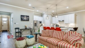A spacious living room with a striped sofa, ottomans, and a coffee table with fruit.