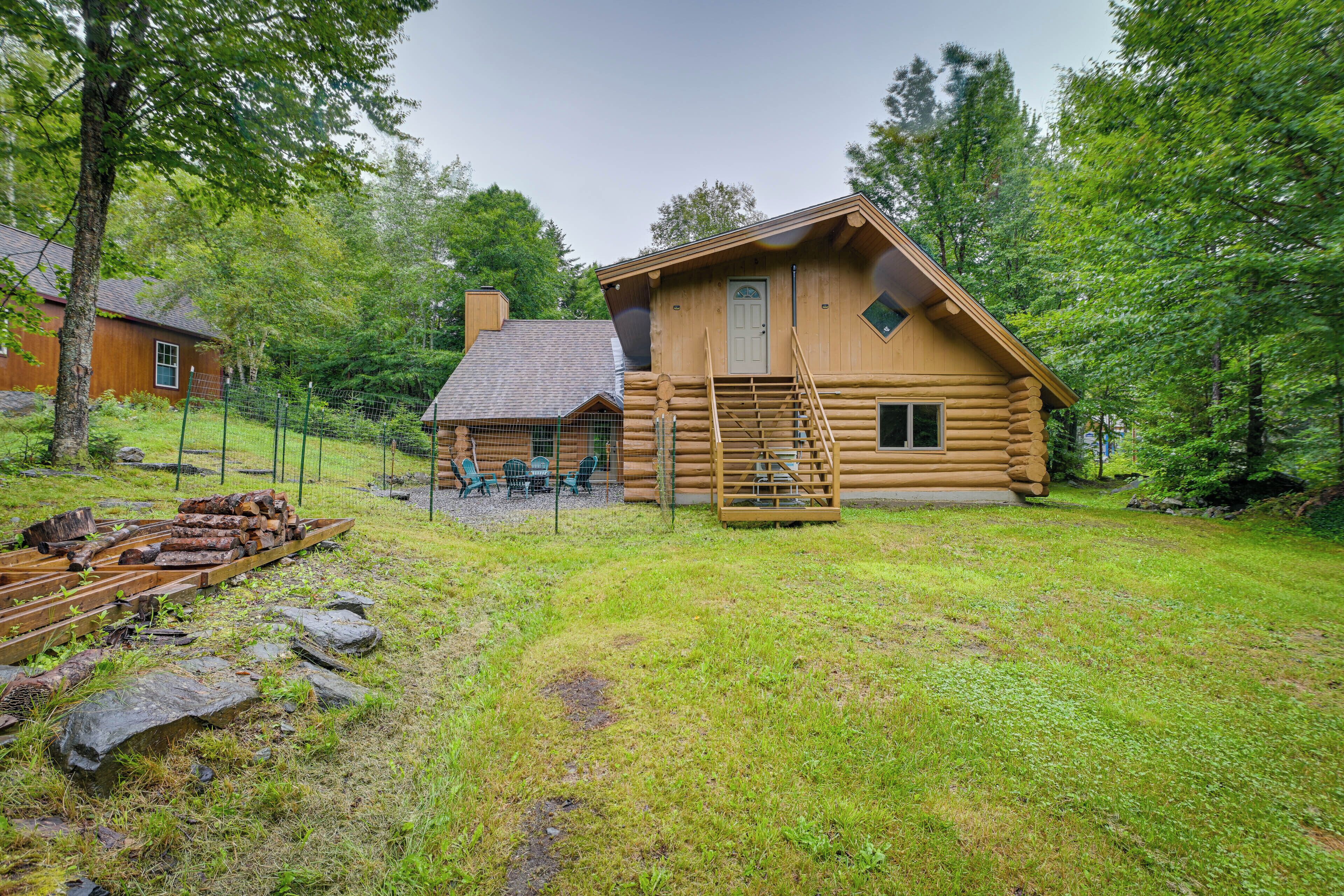 Une cabane en rondins avec une terrasse en bois, une échelle et un petit porche équipé de chaises.